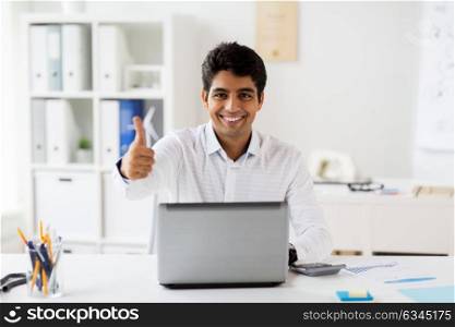 business, people and technology concept - businessman with laptop computer showing thumbs up and papers at office. businessman showing thumbs up at office