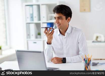 business, people and technology concept - businessman with laptop computer using voice command recorder on smartphone at office. businessman using voice recorder on smartphone