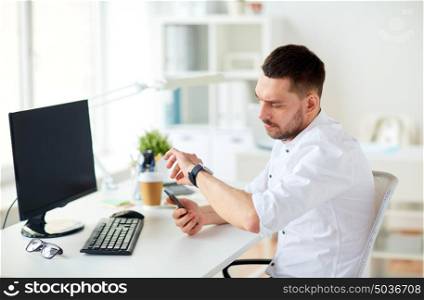 business, people and technology concept - businessman with smartphone and computer at office. businessman with smartphone and computer at office