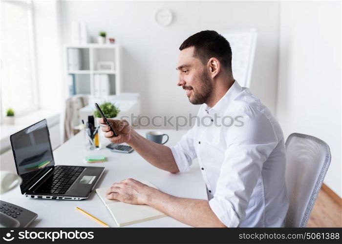 business, people and technology concept - businessman with smartphone, laptop computer and notebook at office. businessman with smartphone and notebook at office