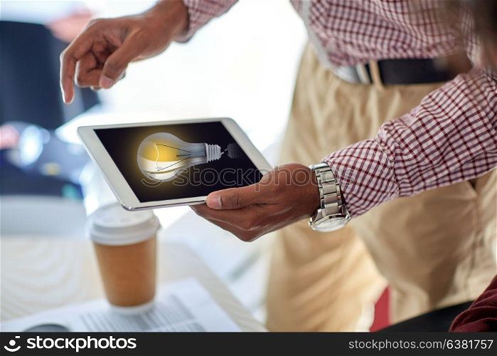 business, people and technology concept - close up of businessman with light bulb on tablet pc computer screen at office. businessman with lightbulb on tablet pc at office