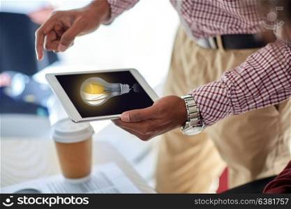 business, people and technology concept - close up of businessman with light bulb on tablet pc computer screen at office. businessman with lightbulb on tablet pc at office