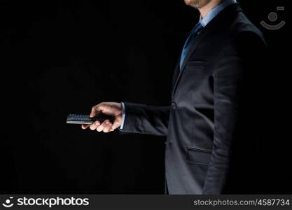 business, people and technology concept - close up of businessman with remote controller over black