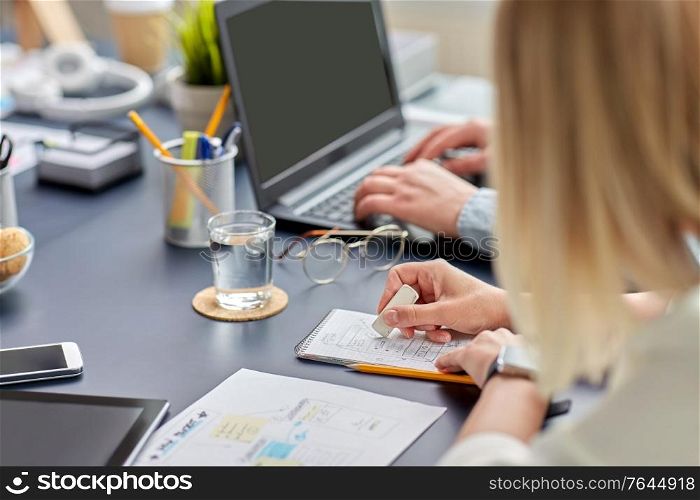 business, people and technology concept - close up of ui designer with notebook and eraser working on mobile app design at office. woman with notebook working on ui design at office