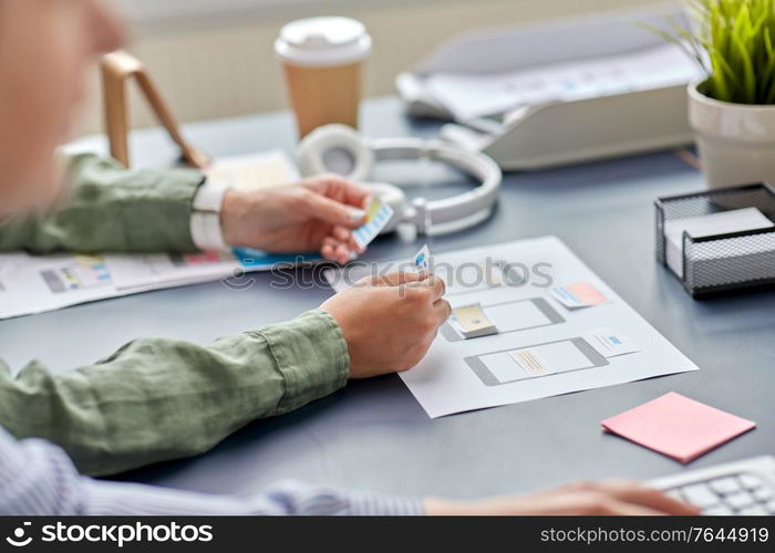 business, people and technology concept - close up of ui designer with mockups working on mobile app design at office. hands with mockup working on ui design at office