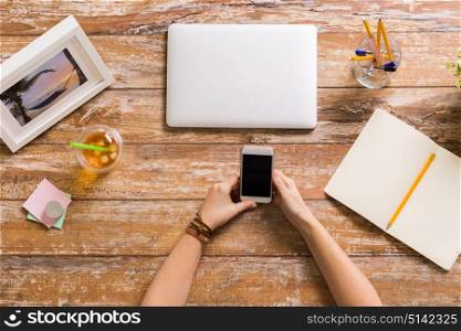 business, people and technology concept - hands with smartphone, notebook and laptop computer at wooden office table. hands with smartphone and laptop at office table