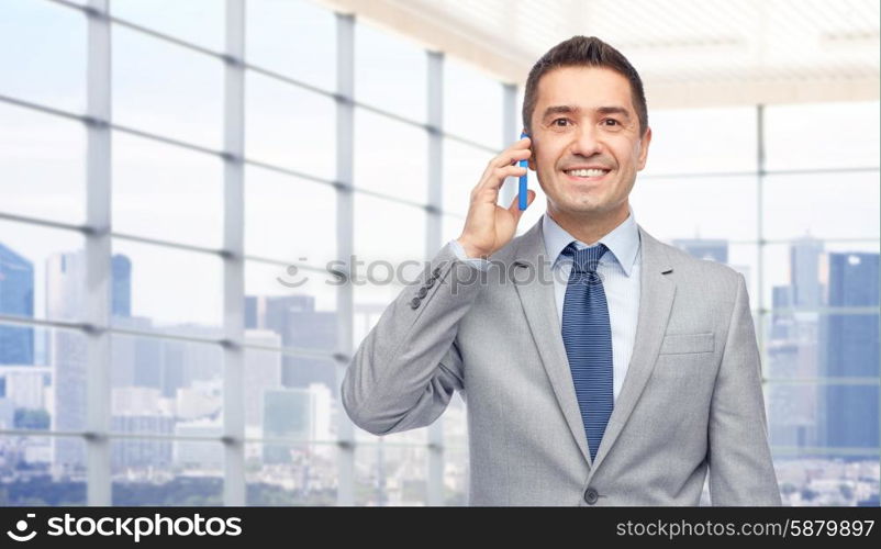 business, people and technology concept -happy businessman calling on smartphone over city office window background