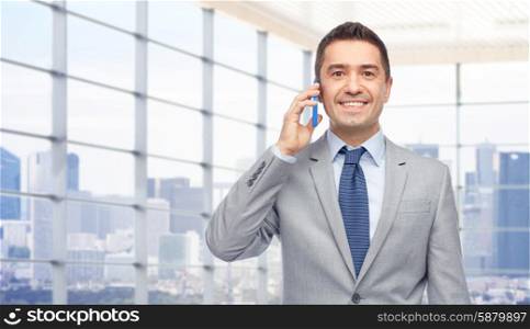business, people and technology concept -happy businessman calling on smartphone over city office window background