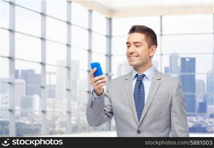 business, people and technology concept -happy businessman texting on smartphone over office room and window with city view background