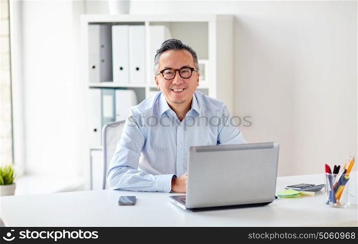 business, people and technology concept - happy smiling businessman in eyeglasses with laptop computer office. happy businessman in eyeglasses with laptop office