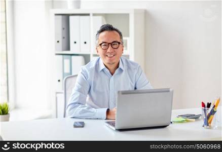business, people and technology concept - happy smiling businessman in eyeglasses with laptop computer office. happy businessman in eyeglasses with laptop office