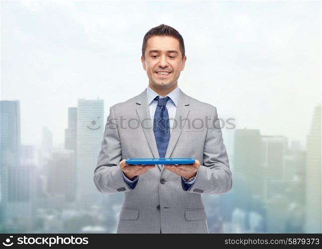 business, people and technology concept - happy smiling businessman in suit holding tablet pc computer over city background