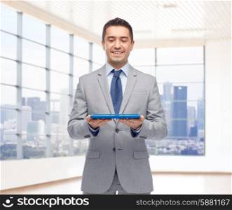 business, people and technology concept - happy smiling businessman in suit holding tablet pc computer over office room background