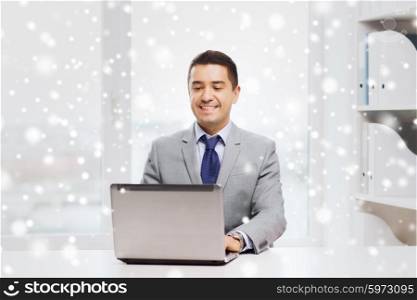 business, people and technology concept - happy smiling businessman in suit working with laptop computer in office over snow effect
