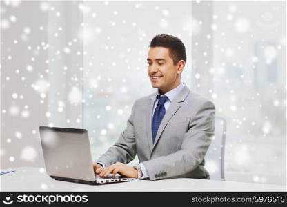 business, people and technology concept - happy smiling businessman in suit working with laptop computer in office over snow effect