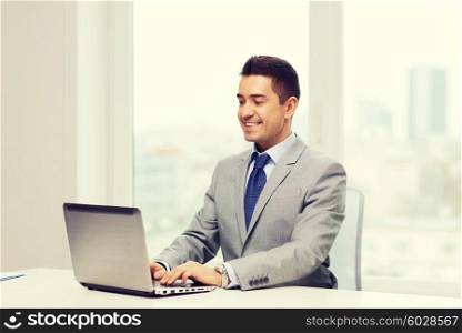 business, people and technology concept - happy smiling businessman in suit working with laptop computer in office