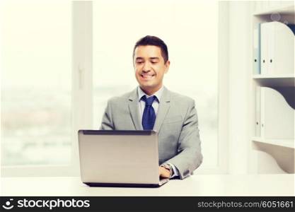 business, people and technology concept - happy smiling businessman in suit working with laptop computer in office