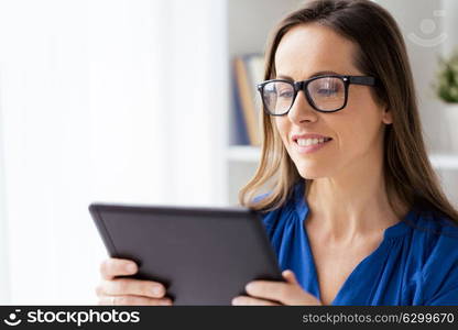 business, people and technology concept - happy smiling businesswoman in glasses with tablet pc computer working at home or office. woman with tablet pc working at home or office