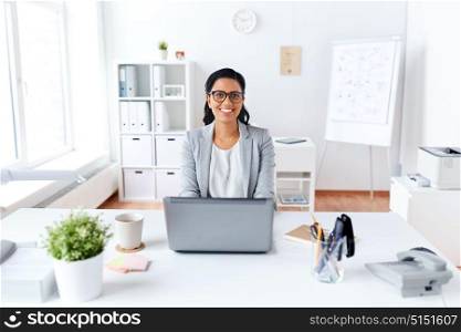 business, people and technology concept - happy smiling businesswoman with laptop computer working at office. happy businesswoman with laptop working at office
