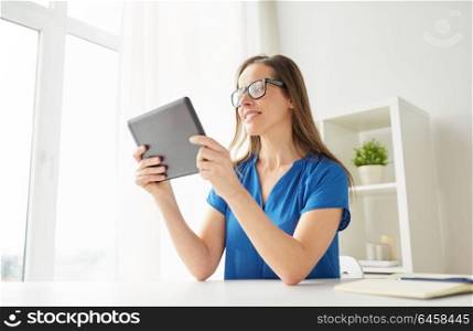 business, people and technology concept - happy smiling middle-aged woman in glasses with tablet pc computer working at home or office. woman with tablet pc working at home or office