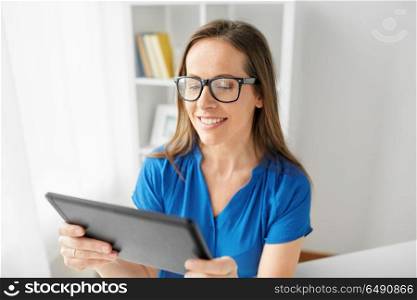 business, people and technology concept - happy smiling middle-aged woman in glasses with tablet pc computer working at home or office. woman with tablet pc working at home or office. woman with tablet pc working at home or office
