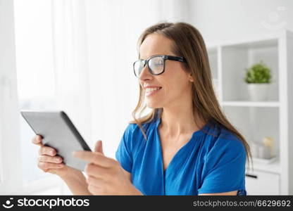 business, people and technology concept - happy smiling middle-aged woman in glasses with tablet pc computer working at home or office. woman with tablet pc working at home or office