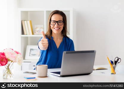 business, people and technology concept - happy smiling woman in glasses with laptop computer showing thumbs up at office. woman with laptop showing thumbs up at office