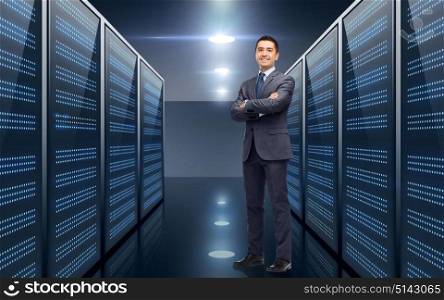 business, people and technology concept - smiling businessman in suit over server room background. smiling businessman over server room background
