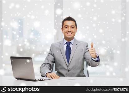 business, people and technology concept - smiling businessman in suit working with laptop computer in office over snow effect