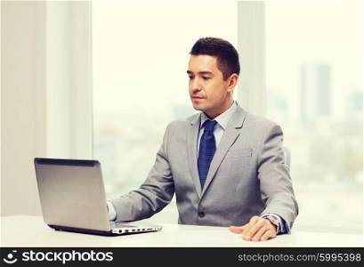 business, people and technology concept - smiling businessman in suit working with laptop computer in office