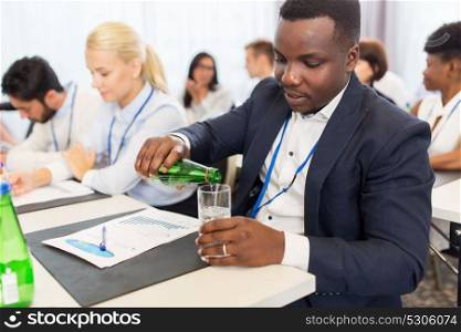 business, people and thirst concept - young businessman pouring himself drinking water in a glass at conference. businessman drinking water at business conference