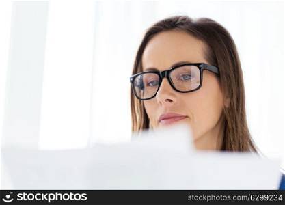 business, people and work concept - businesswoman in glasses reading documents at office. businesswoman in glasses reading papers at office