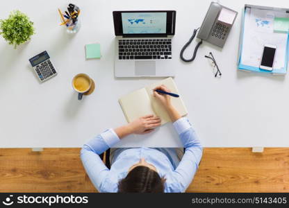 business, people and work concept - businesswoman with laptop computer writing to notebook at office. businesswoman writing to notebook at office