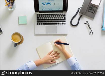 business, people and work concept - hands of businesswoman with laptop computer writing to notebook at office. businesswoman hands writing to notebook at office