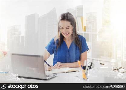 business, people and work concept - happy smiling woman with laptop computer working and writing to notebook at office over city buildings background and double exposure effect. happy woman writing to notebook at office