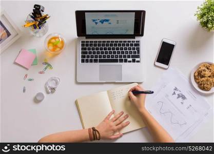 business, people and work concept - woman hands with laptop computer writing to notebook at office table. hands with laptop writing to notebook at office