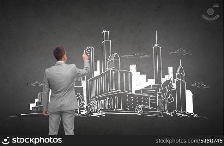 business, people, architecture and real estate concept - businessman drawing city sketch from back over dark gray concrete wall background