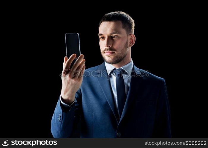 business, people, augmented reality and modern technology concept - businessman in suit working with transparent smartphone over black background. businessman with transparent smartphone