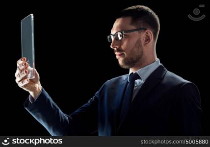 business, people, augmented reality and modern technology concept - businessman in suit working with transparent tablet pc computer over black background. businessman in suit with transparent tablet pc