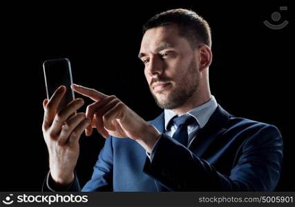 business, people, augmented reality and modern technology concept - businessman in suit working with transparent smartphone over black background. businessman with transparent smartphone
