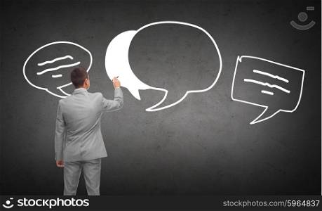 business, people, communication and information concept - businessman drawing text bubbles from back over dark gray concrete wall background