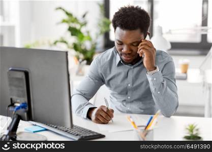 business, people, communication and technology concept - african american businessman with papers and computer calling on smartphone at office. businessman calling on smartphone at office. businessman calling on smartphone at office