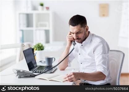 business, people, communication and technology concept - businessman calling on phone and writing to notebook at office. businessman with pad calling on phone at office