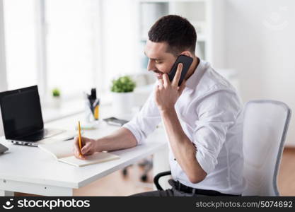 business, people, communication and technology concept - businessman calling on smartphone and writing to notebook at office. businessman calling on smartphone at office