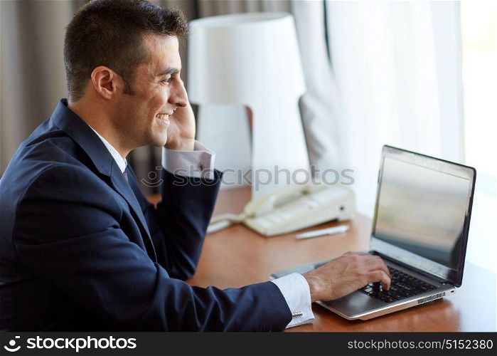 business, people, communication and technology concept - businessman with laptop computer calling on smartphone at hotel room. businessman with laptop and smartphone at hotel
