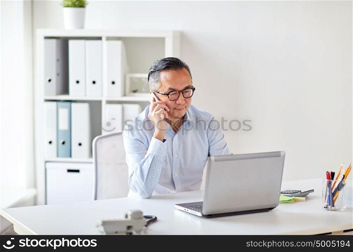 business, people, communication and technology concept - businessman with laptop computer calling on smartphone at office. businessman with laptop calling on smartphone