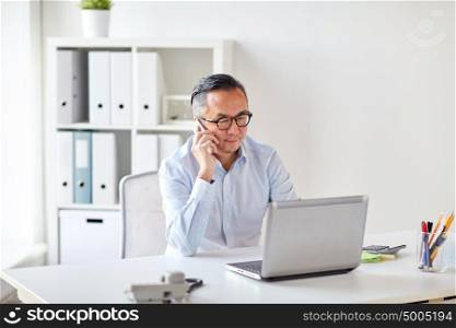business, people, communication and technology concept - businessman with laptop computer calling on smartphone at office. businessman with laptop calling on smartphone