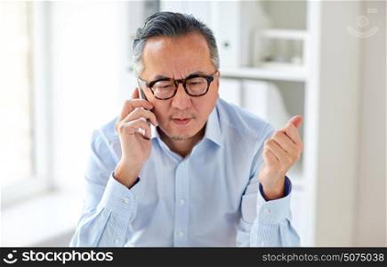 business, people, communication and technology concept - serious asian businessman calling on smartphone in office. businessman calling on smartphone