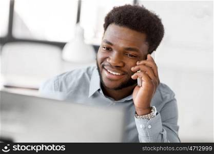 business, people, communication and technology concept - smiling african american businessman with computer calling on smartphone at office. businessman calling on smartphone at office. businessman calling on smartphone at office
