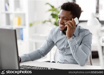 business, people, communication and technology concept - smiling african american businessman with computer calling on smartphone at office. businessman calling on smartphone at office